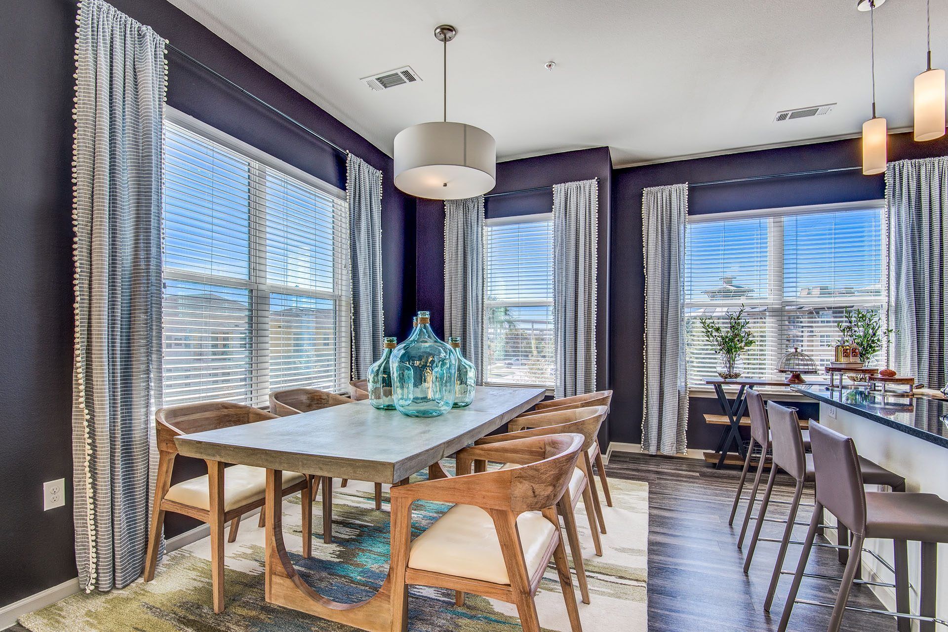 Dining room with a long table, wood chairs, dark blue walls, and large windows with curtains.