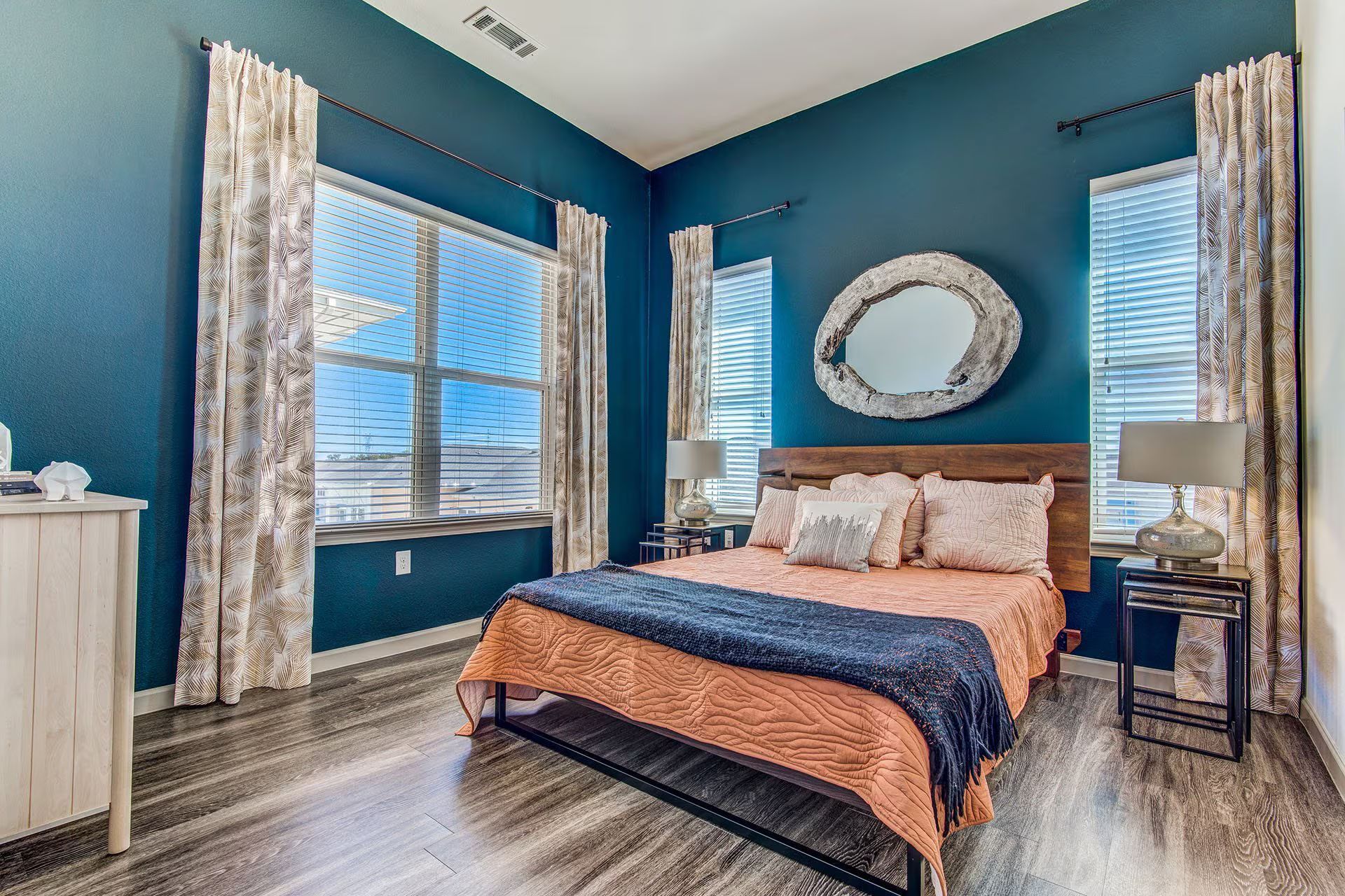 Bedroom with blue walls, wooden headboard, large mirror, and patterned curtains.