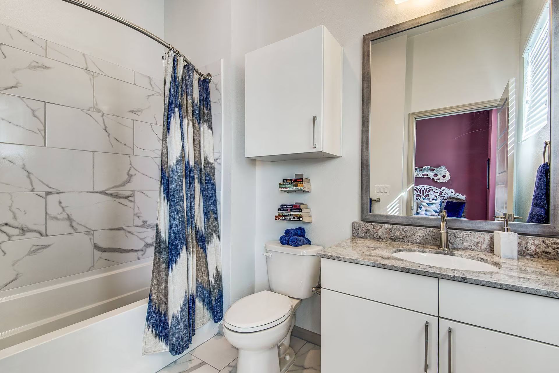 Bathroom with marble-look shower, white vanity, and patterned blue shower curtain. Mirror reflects a purple wall.