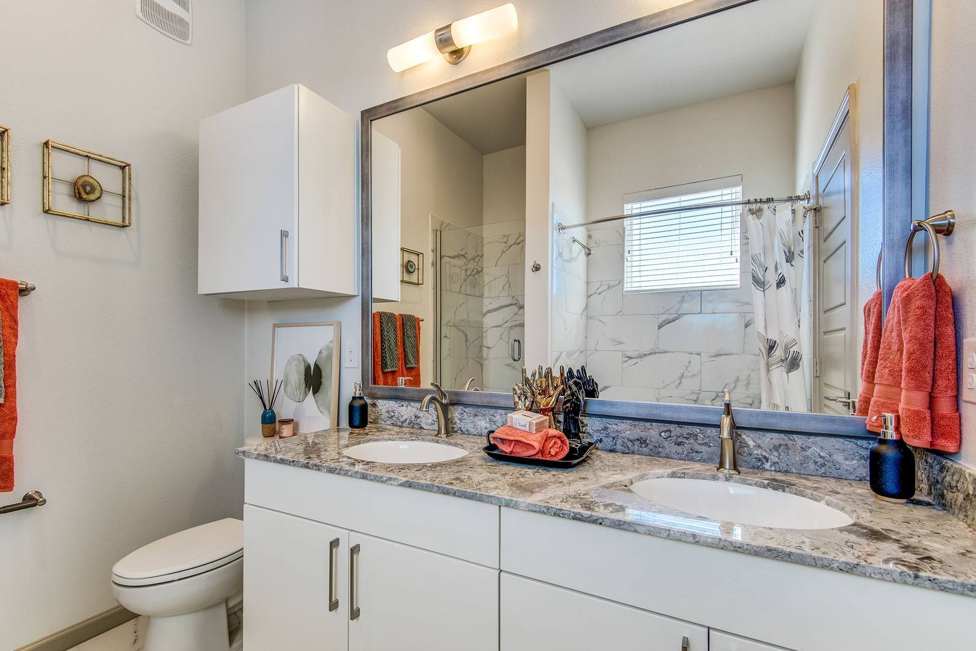 Bathroom with double sinks, white cabinets, large mirror, shower, and a window.