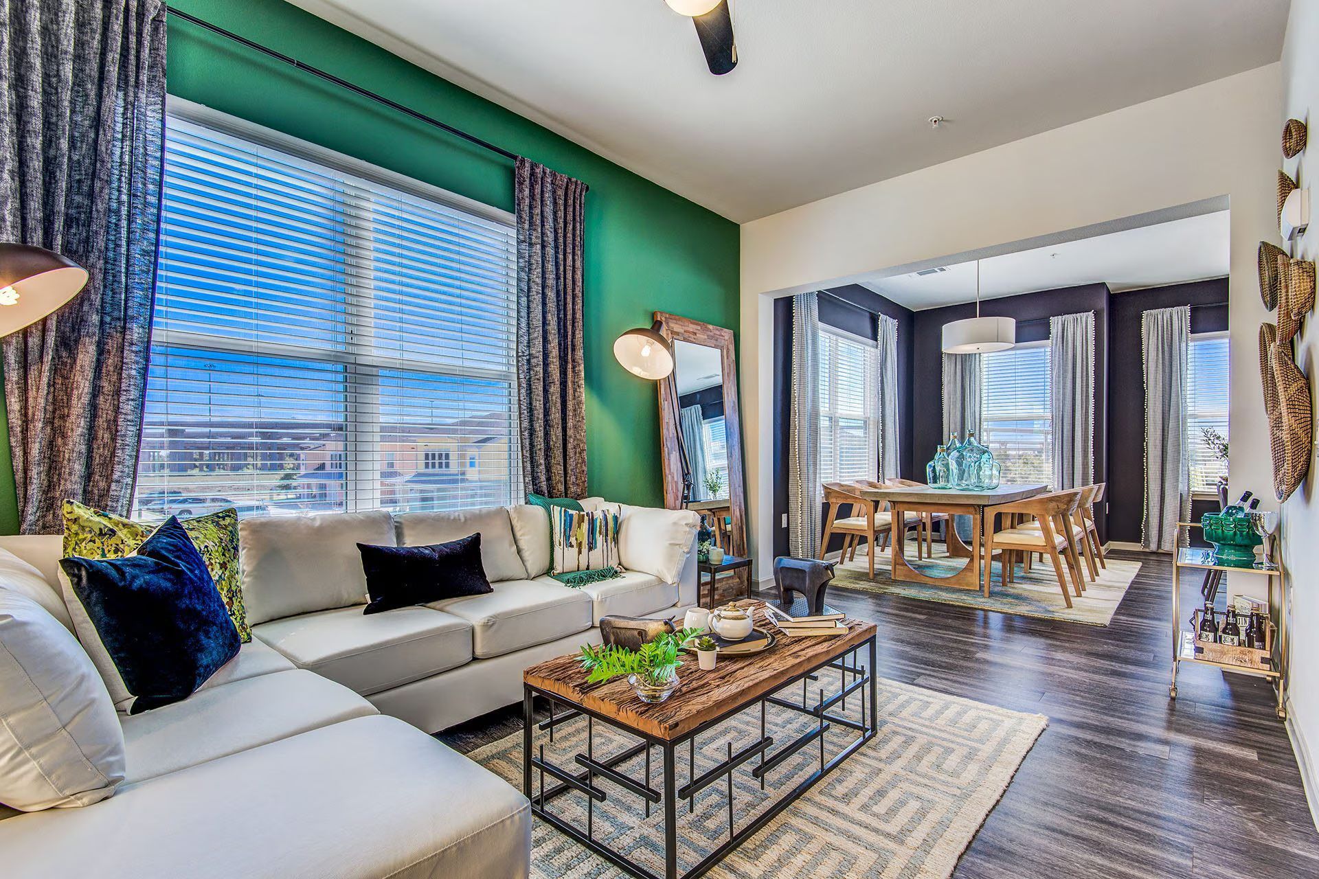 Cozy living room with a white sectional, green accent wall, and open dining area.
