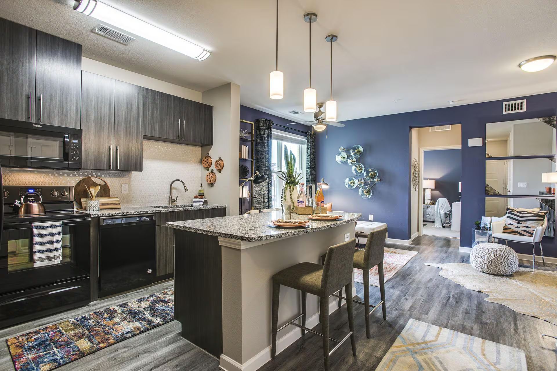 Modern apartment kitchen with dark cabinets, a granite island, and blue accent wall.