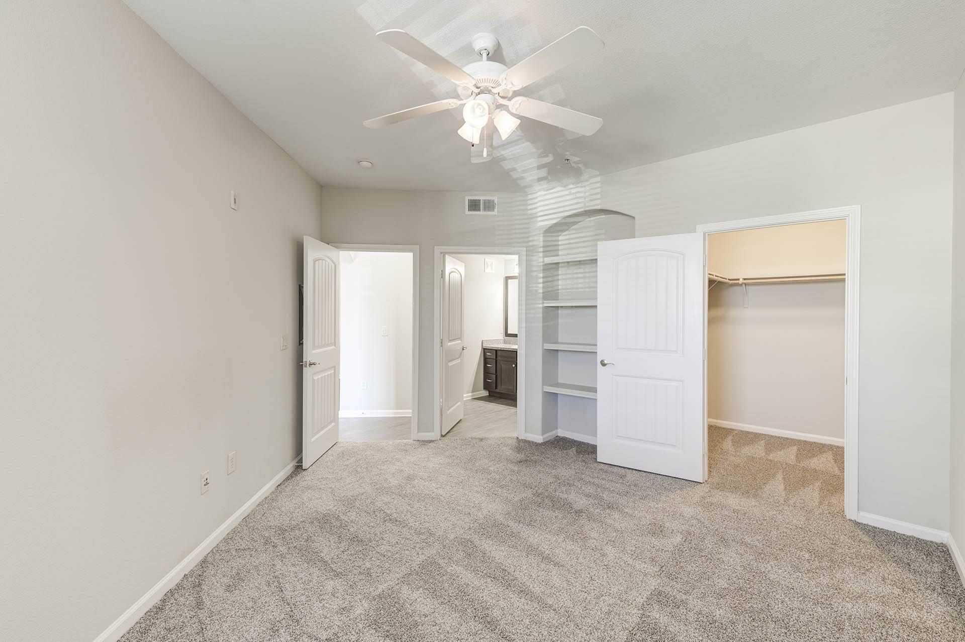 Empty bedroom with white walls, carpet, doors, and a ceiling fan.