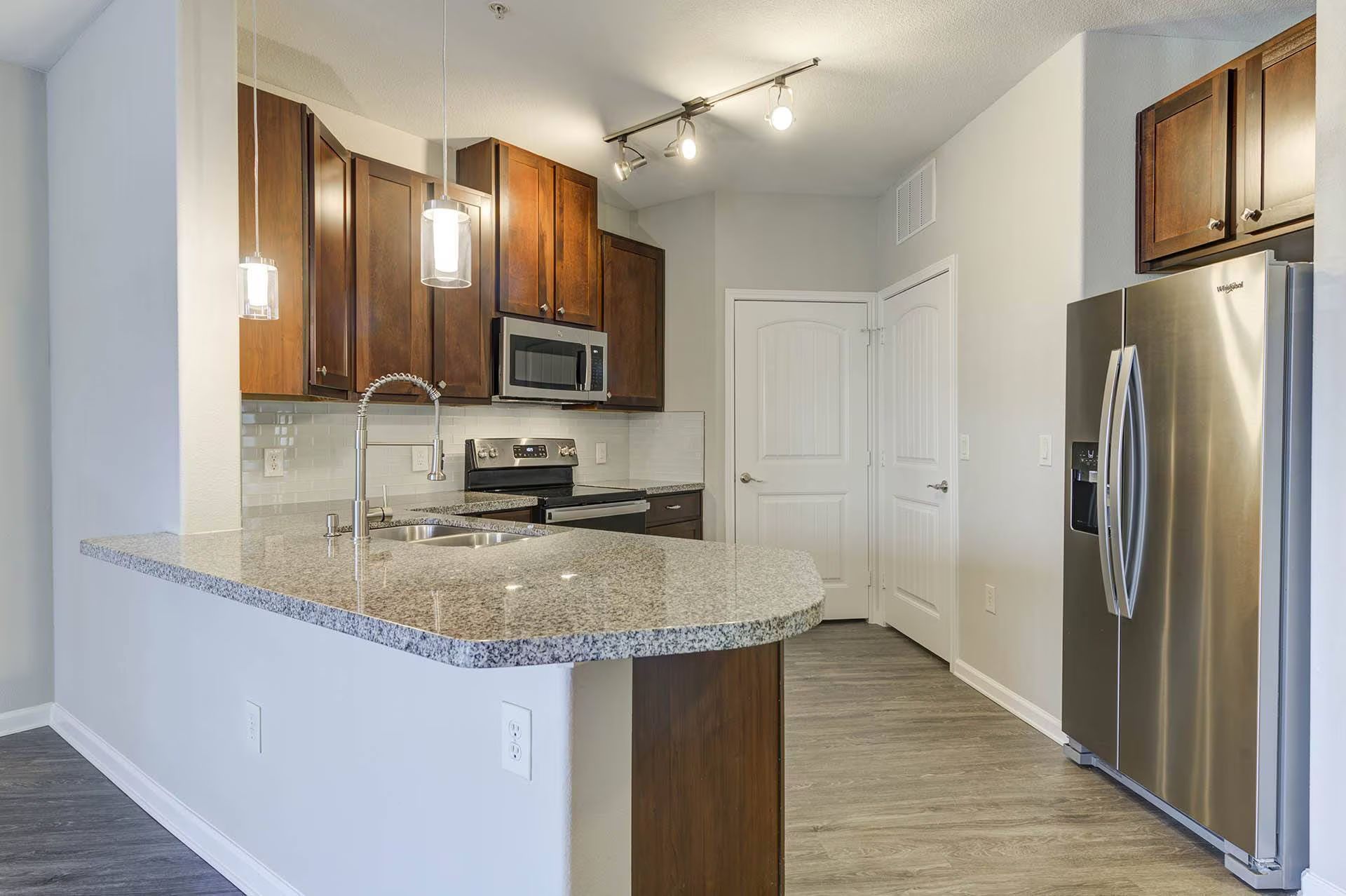 Kitchen with granite countertop, dark wood cabinets, stainless steel fridge, and pendant lights.