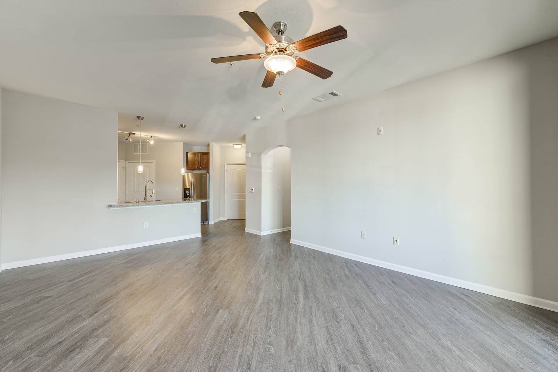 Empty living room with gray wood-look flooring, white walls, and a ceiling fan.