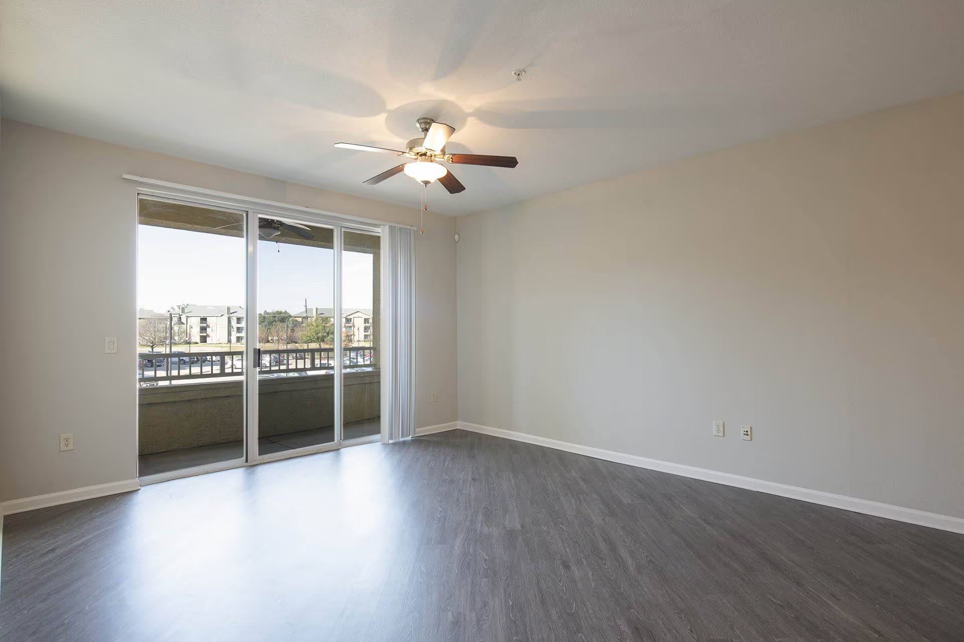 Empty room with large sliding glass doors, balcony view, ceiling fan, and gray flooring.