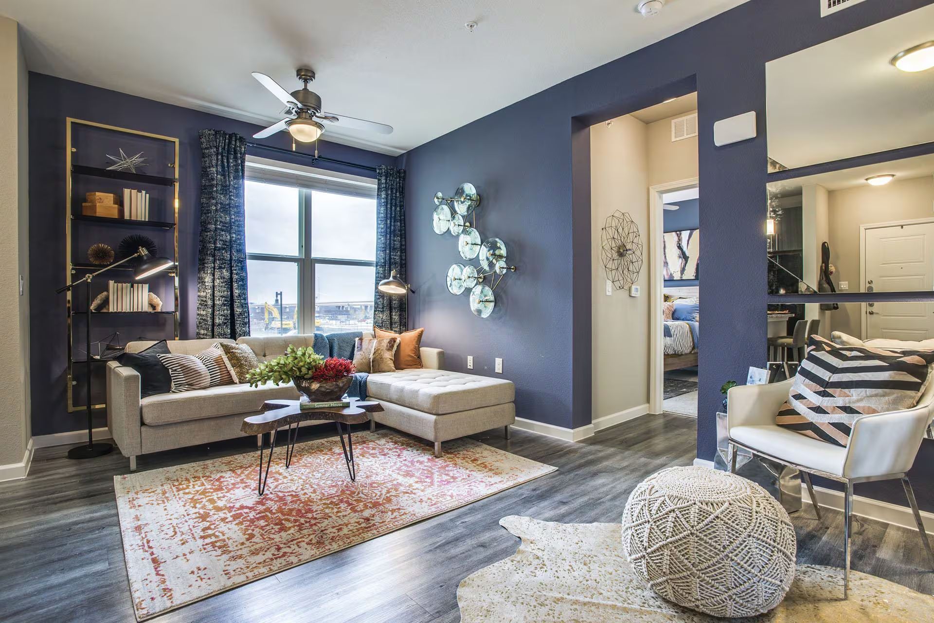 Living room with blue walls, couch, rug, ottoman, large window, and decorative accents.