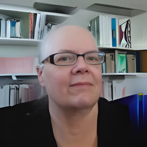 Woman with glasses in front of a bookshelf, wearing black, looking towards the viewer.