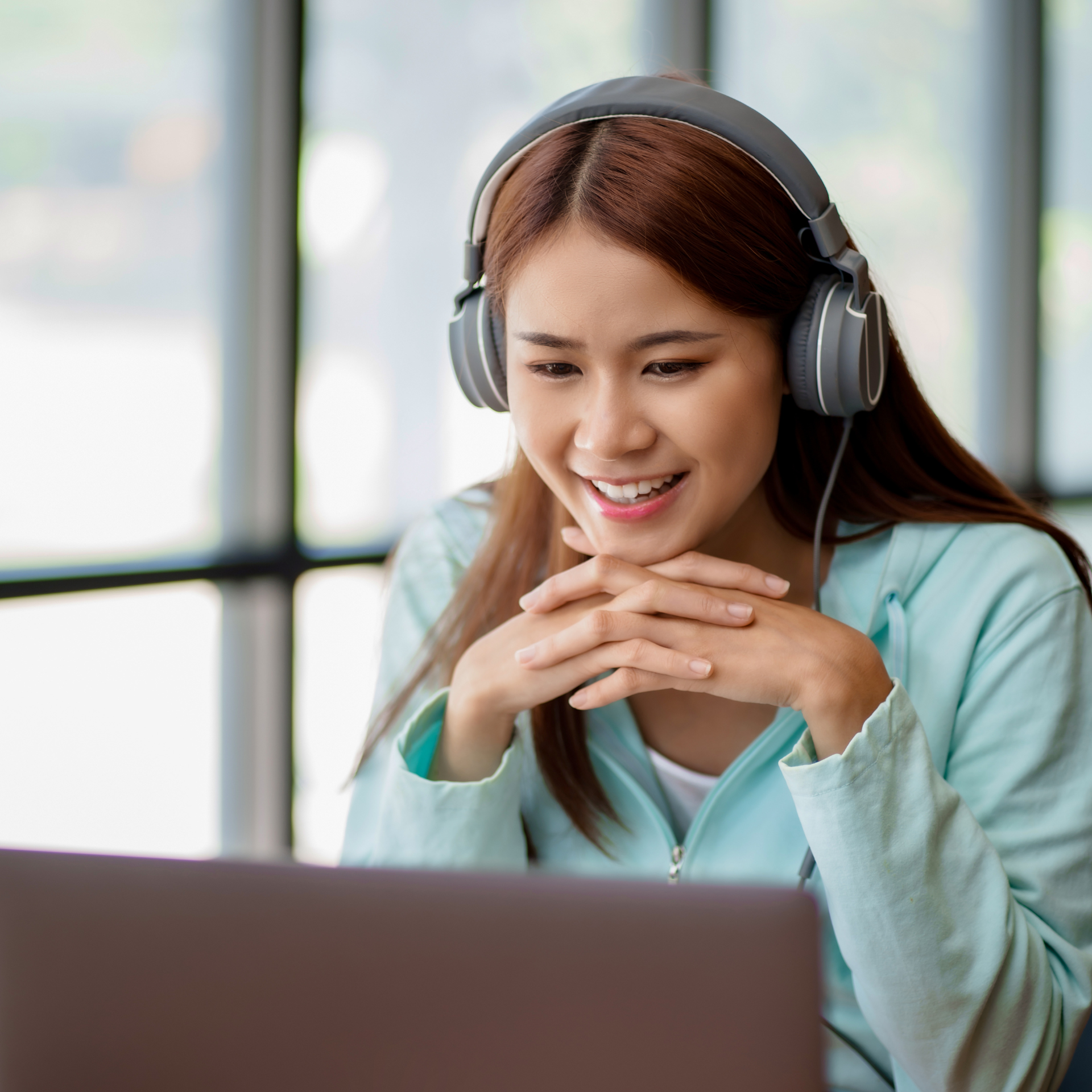 Young woman with headphones smiles while looking at a laptop screen.