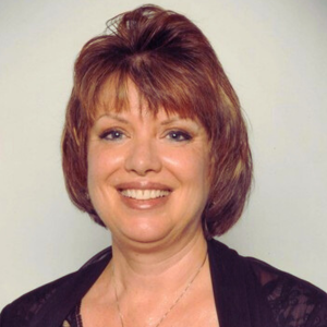 Woman with auburn hair, smiling, wearing a black top, against a white background.