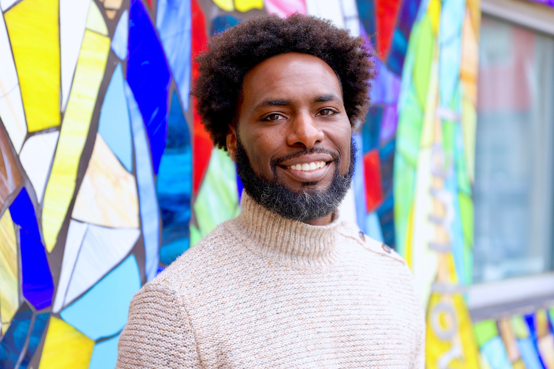 A man with a beard is smiling in front of a stained glass window.