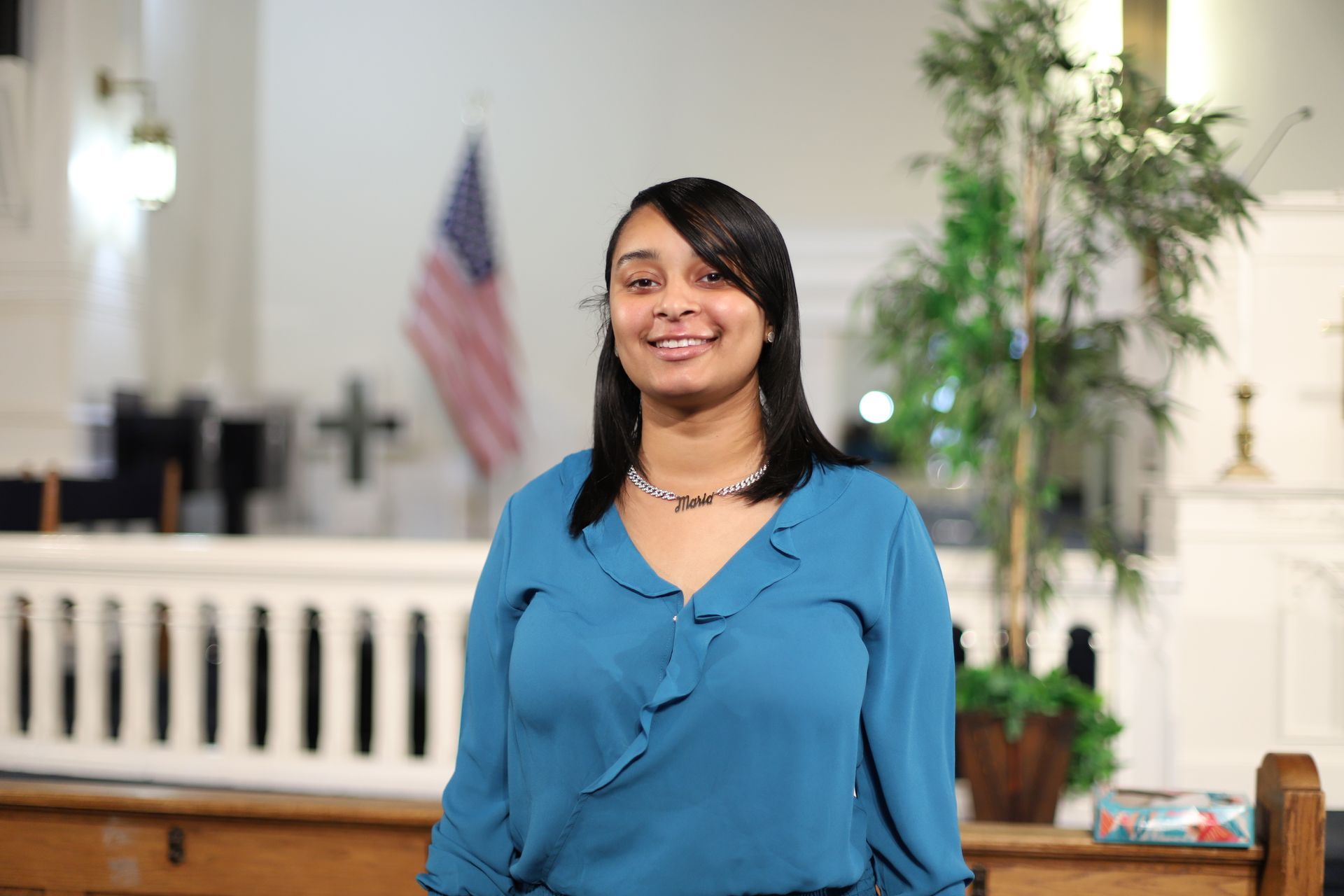 A woman in a blue shirt is standing in a church and smiling.