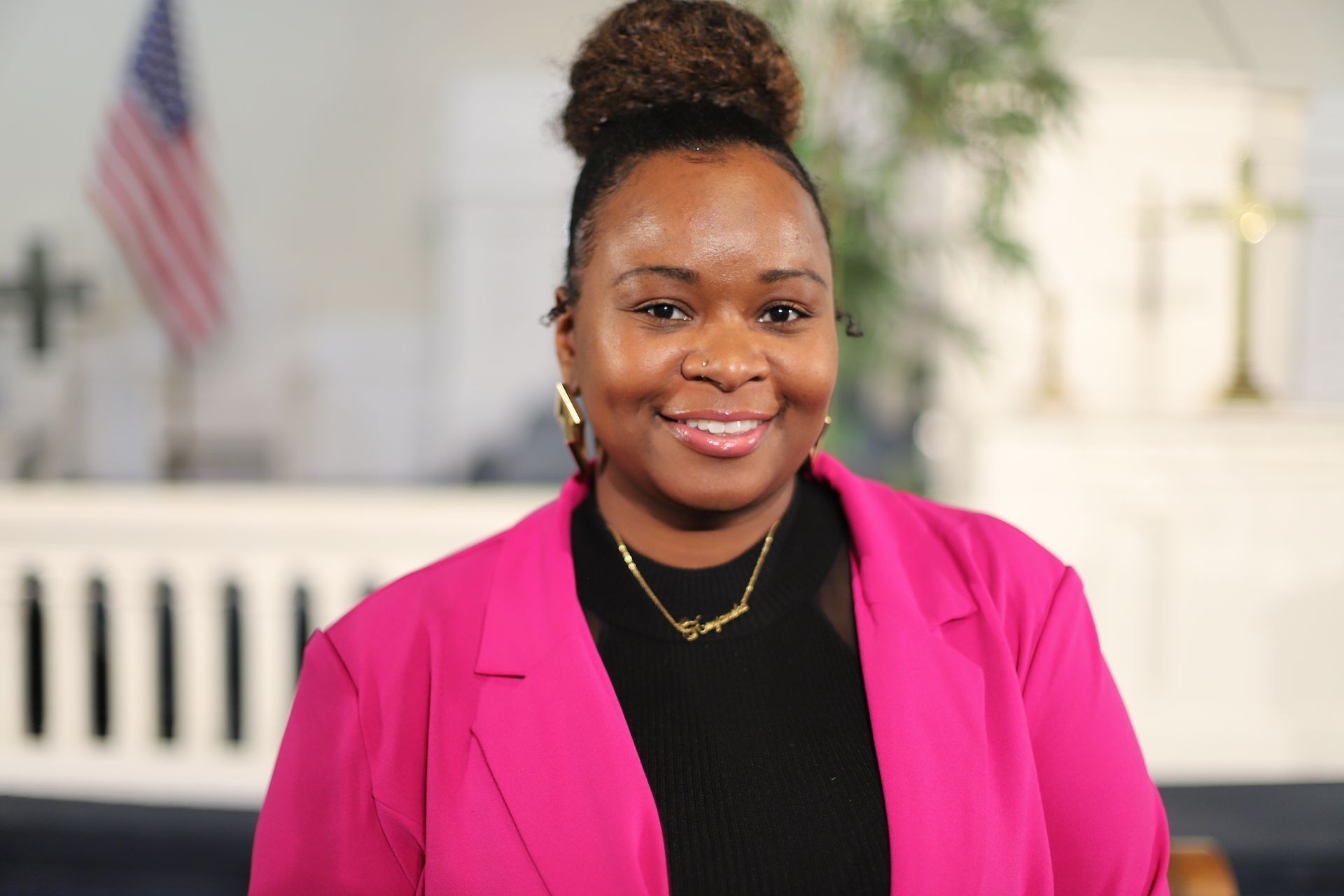 A woman in a pink jacket and black shirt is smiling for the camera.