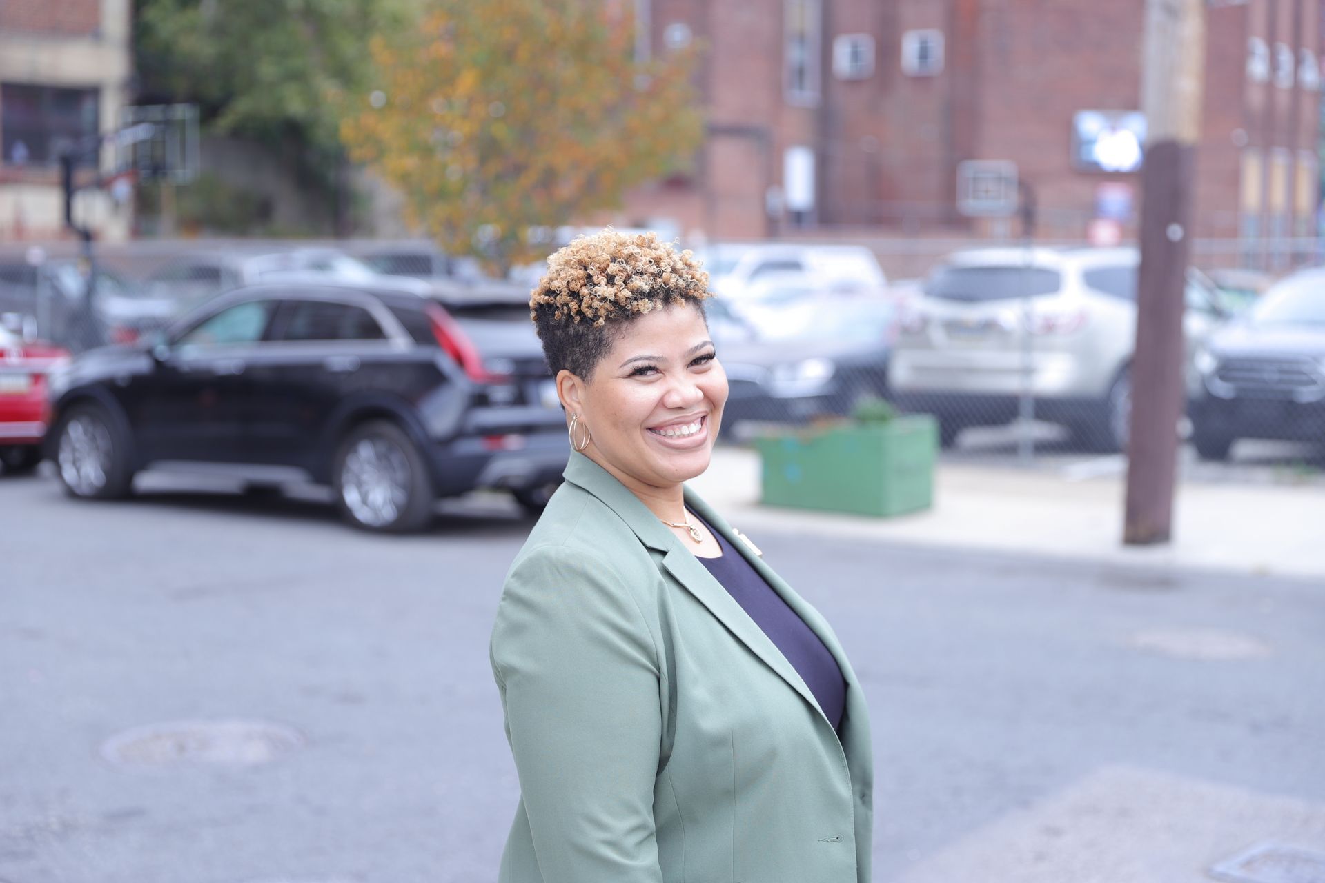 A woman in a green jacket is standing in front of a parking lot.