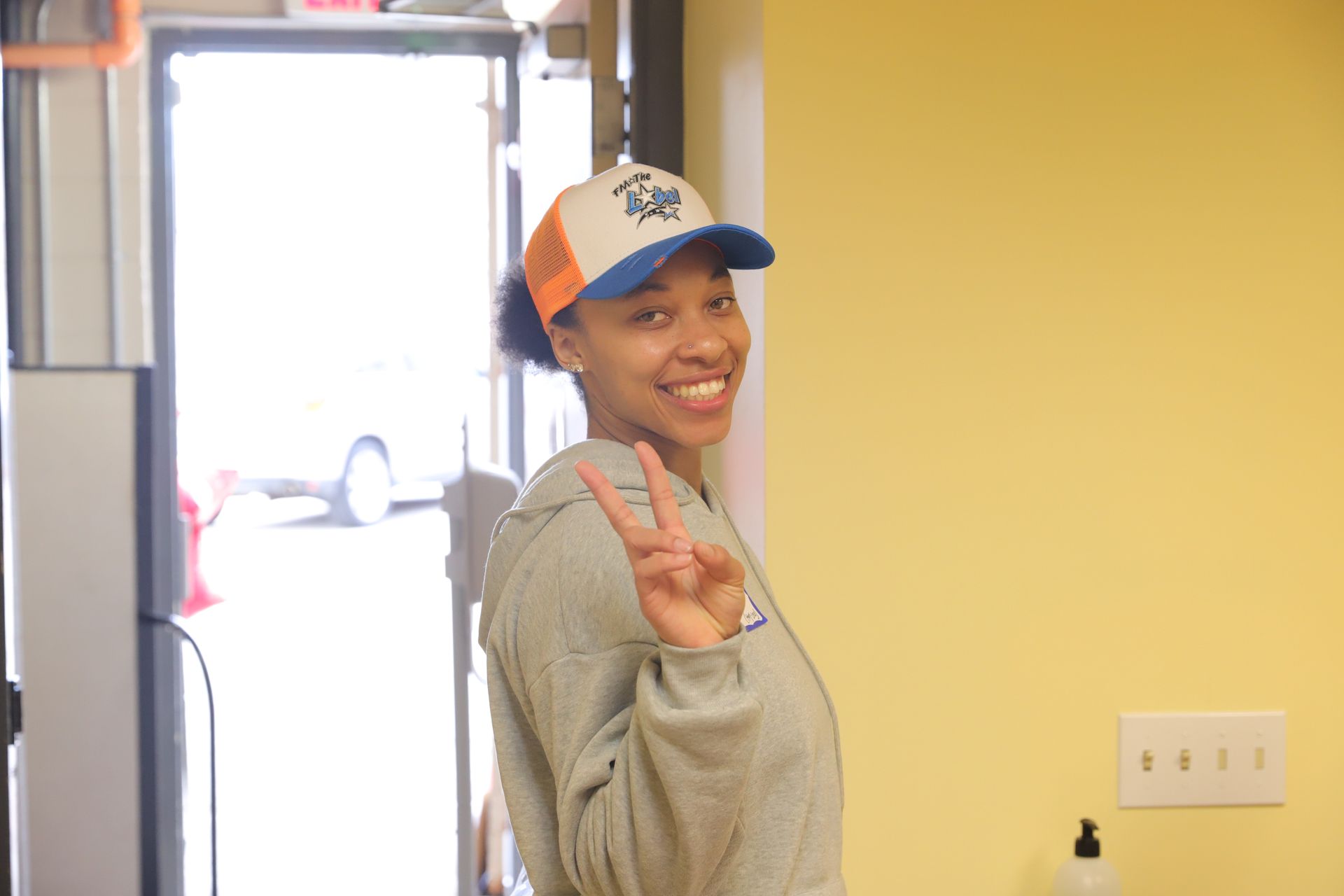 A woman wearing a hat is giving a peace sign.