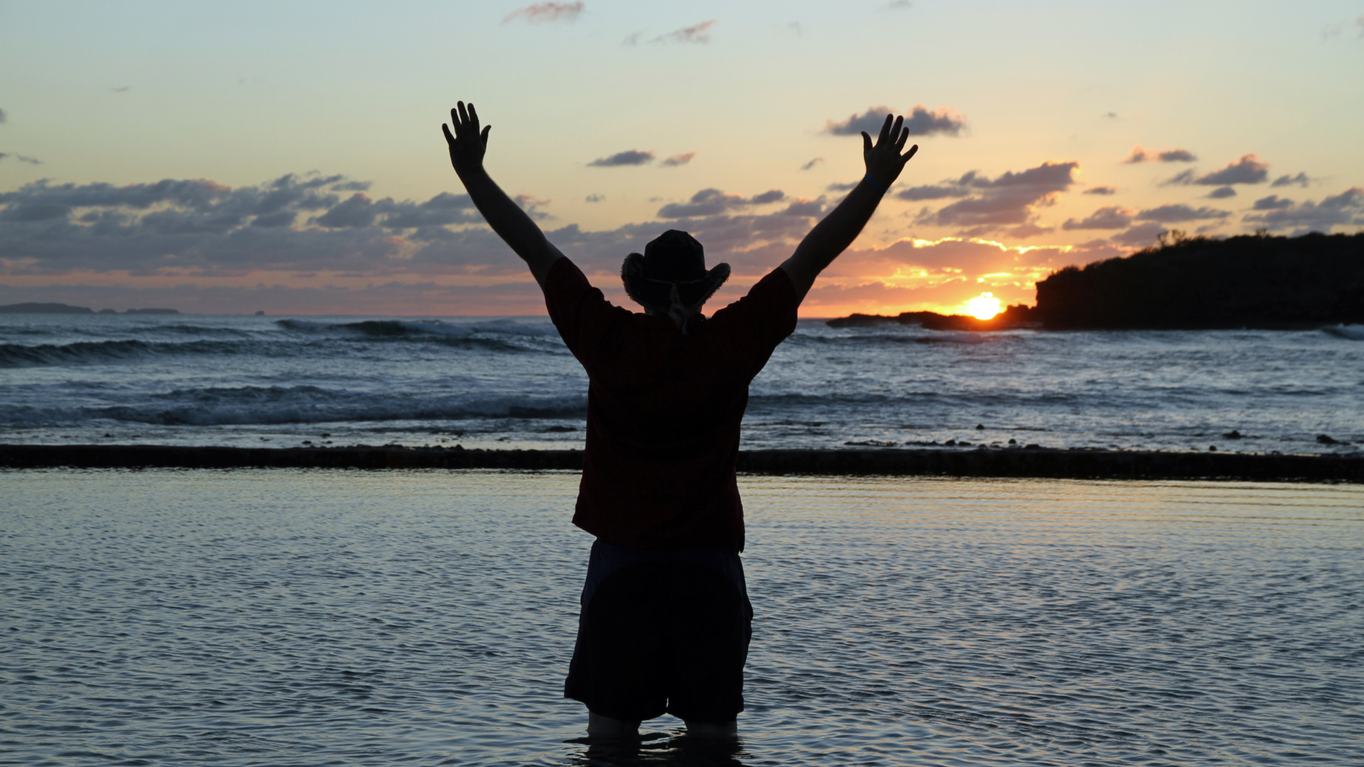 A man stands on a beach with his arms in the air