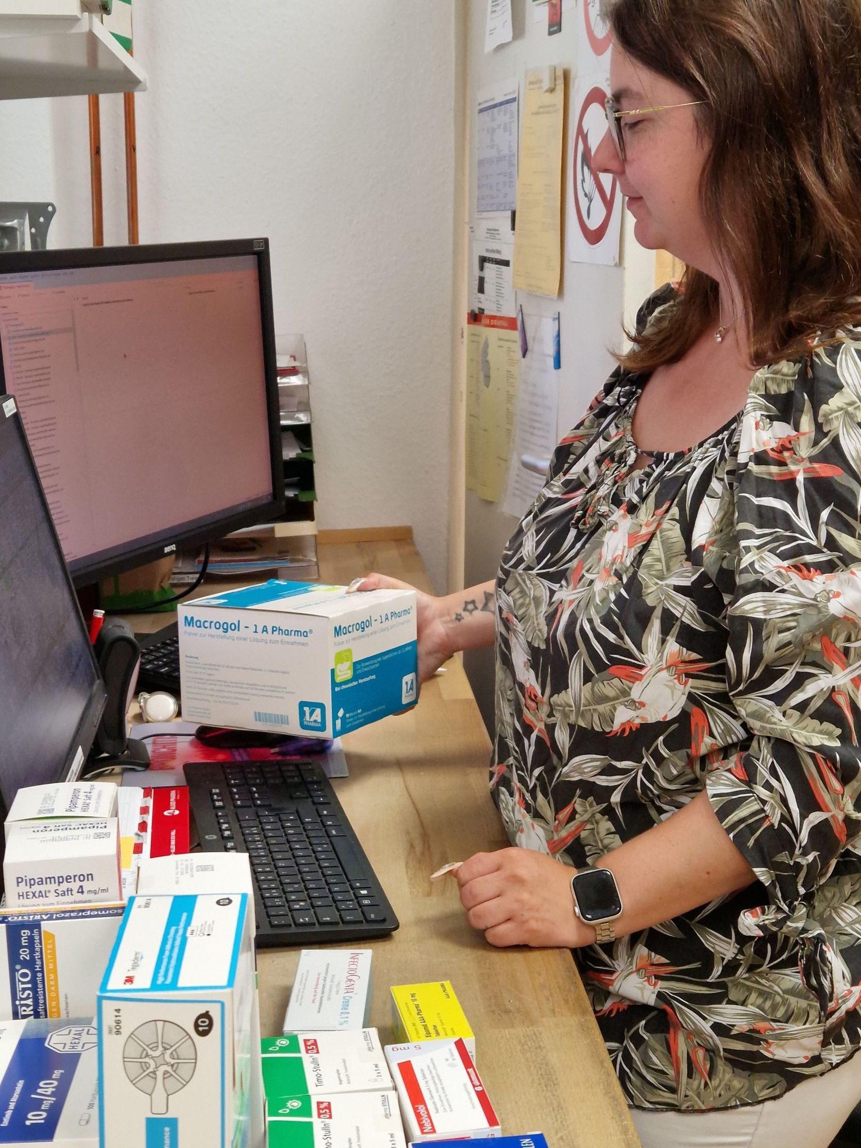 Eine Frau sitzt an einem Schreibtisch vor einem Computer und hält eine Schachtel in der Hand.