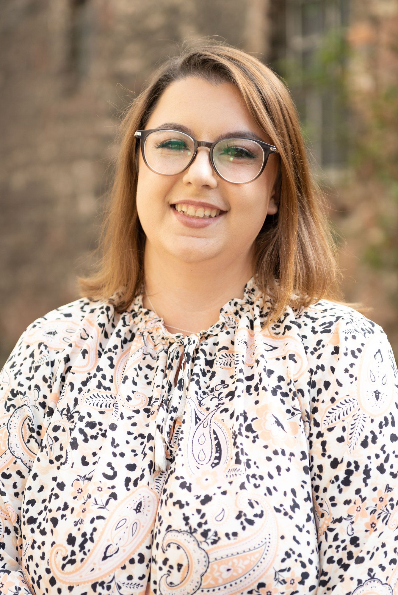 Eine Frau mit Brille und Paisley-Hemd lächelt in die Kamera.