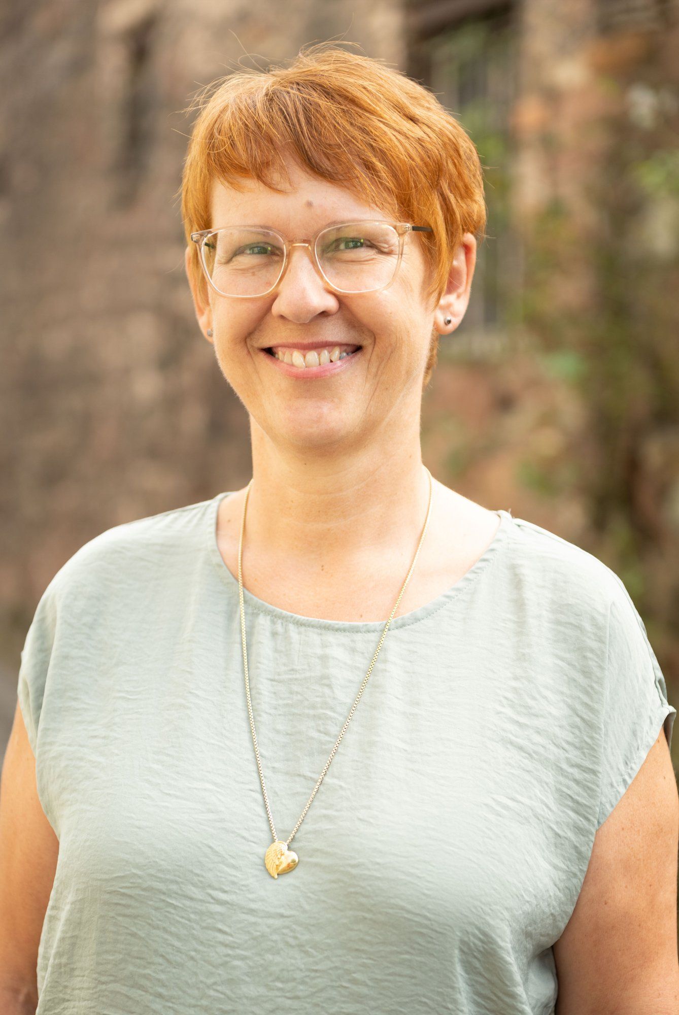 Eine Frau mit Brille und Halskette lächelt in die Kamera.