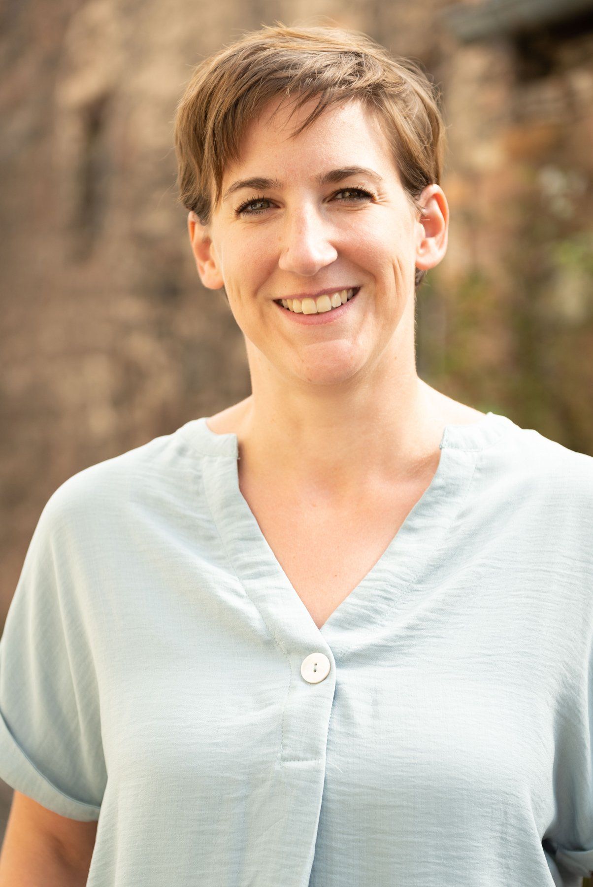 Eine Frau in einem blauen Hemd lächelt in die Kamera.