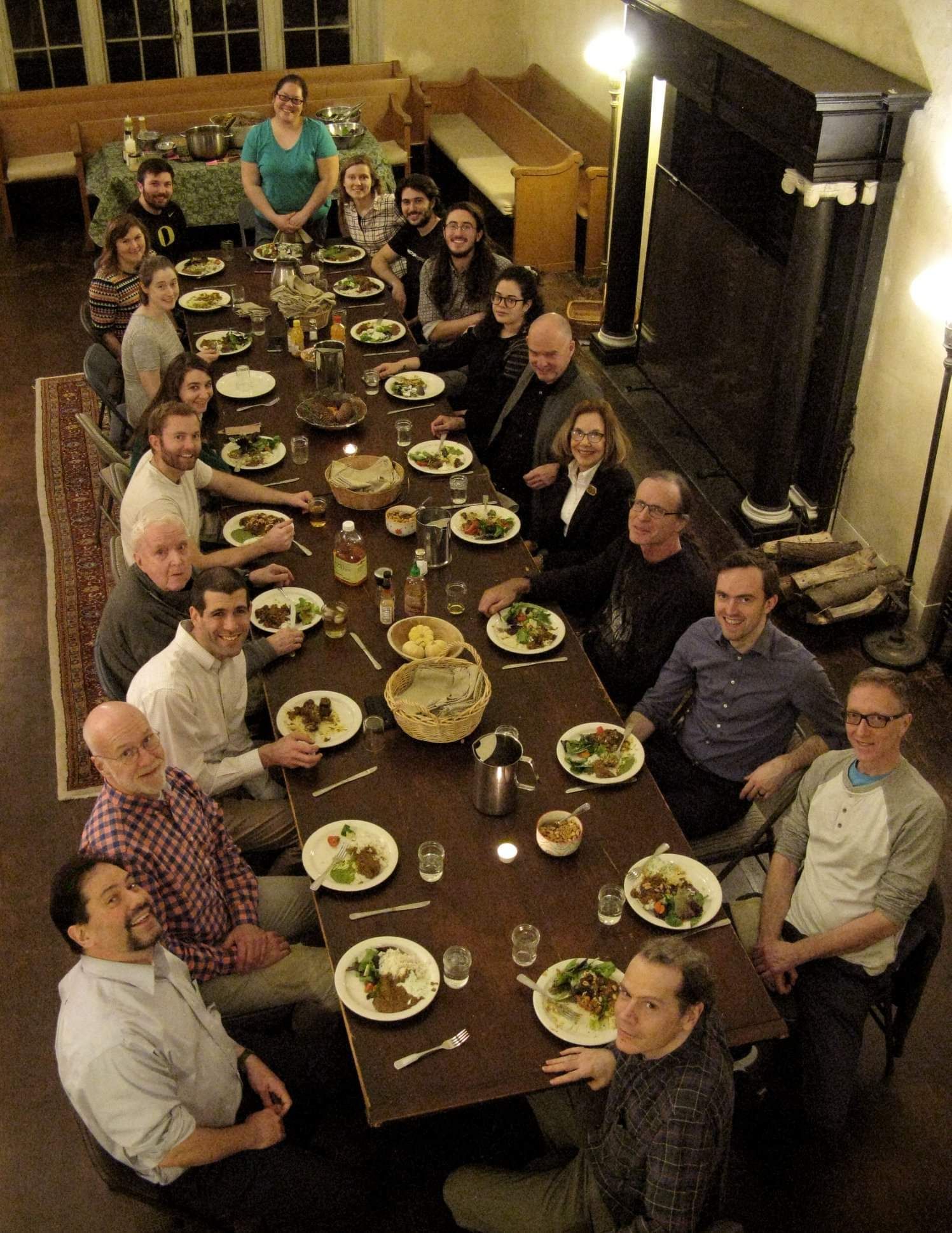 A group of people sitting at a long, candlelit dining table in a rustic room for a shared meal.