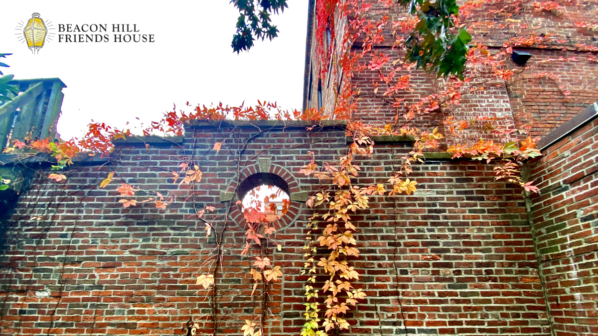 A historic brick wall with a circular window opening, partially covered in vibrant orange and red autumn ivy.