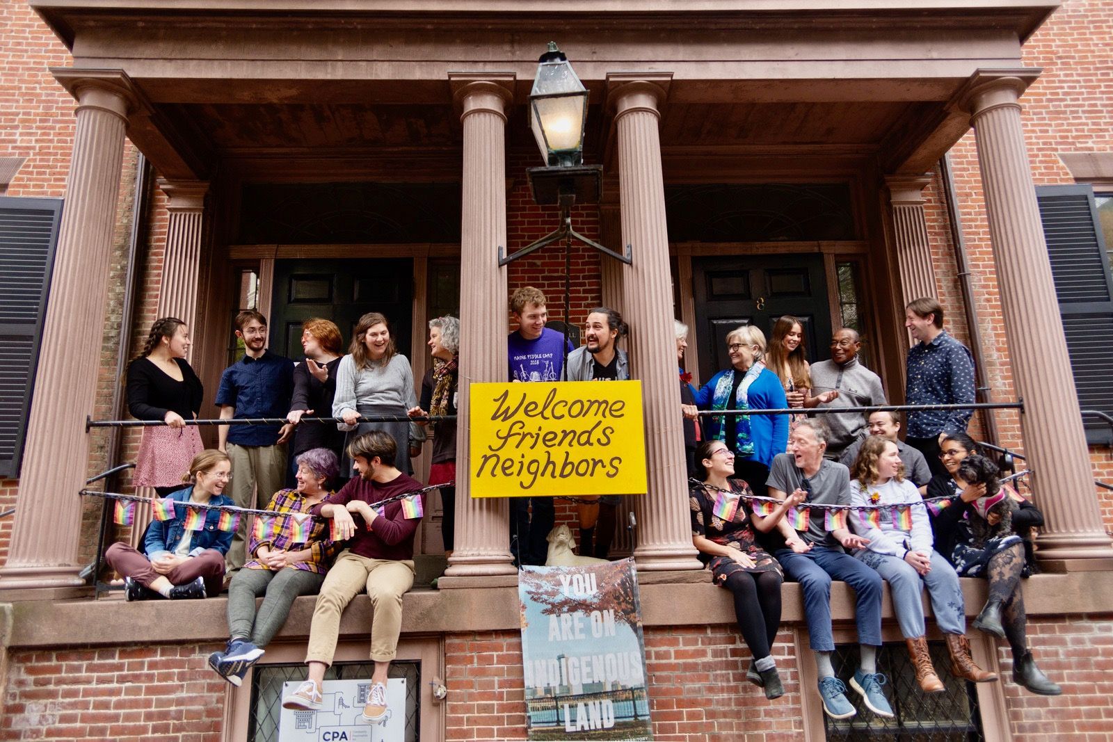 Group of BHFH residents on a balcony, holding a "Welcome Friends Neighbors" sign.