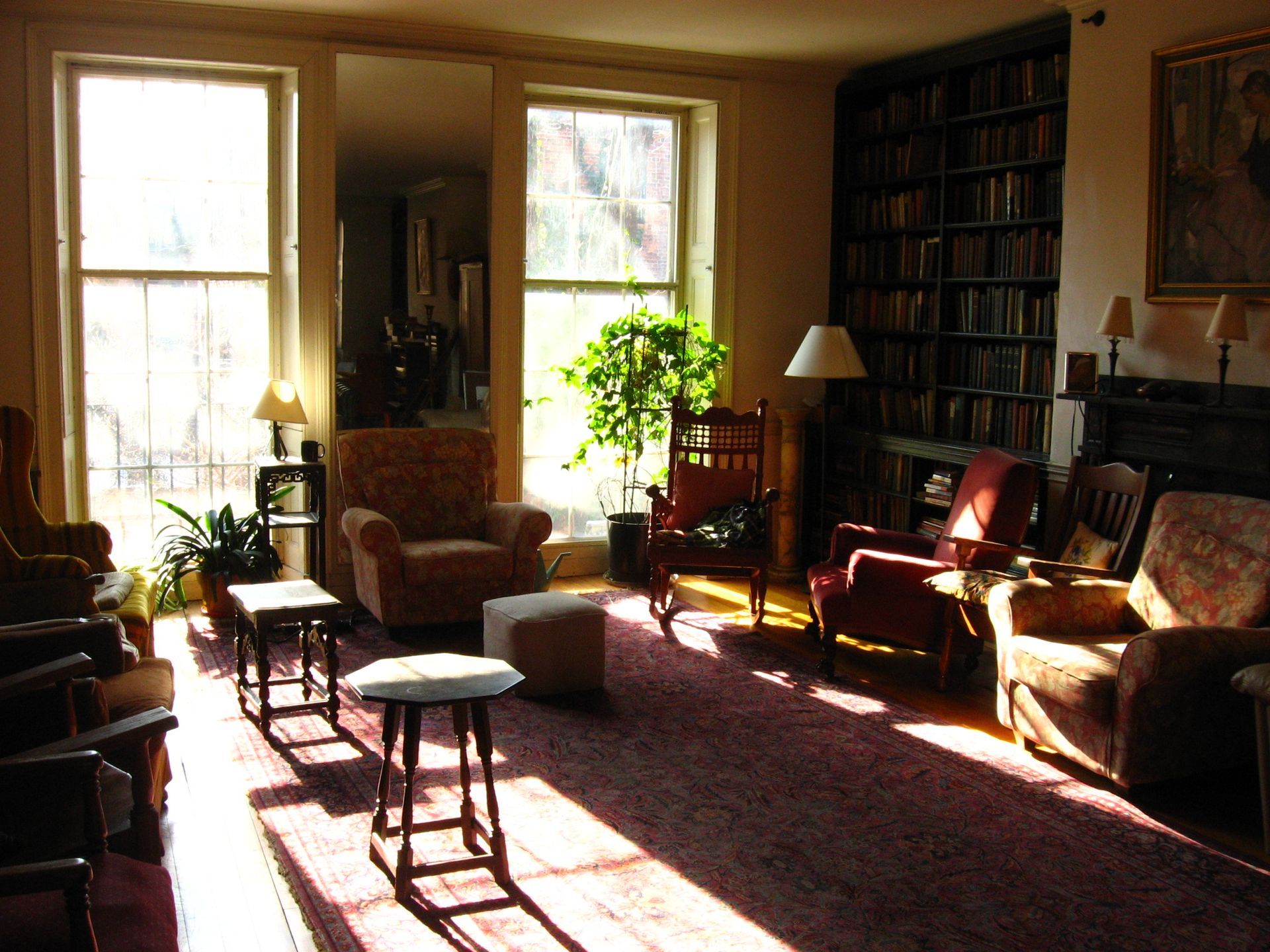 Sunlit library with chairs, bookshelves, rug, and windows.