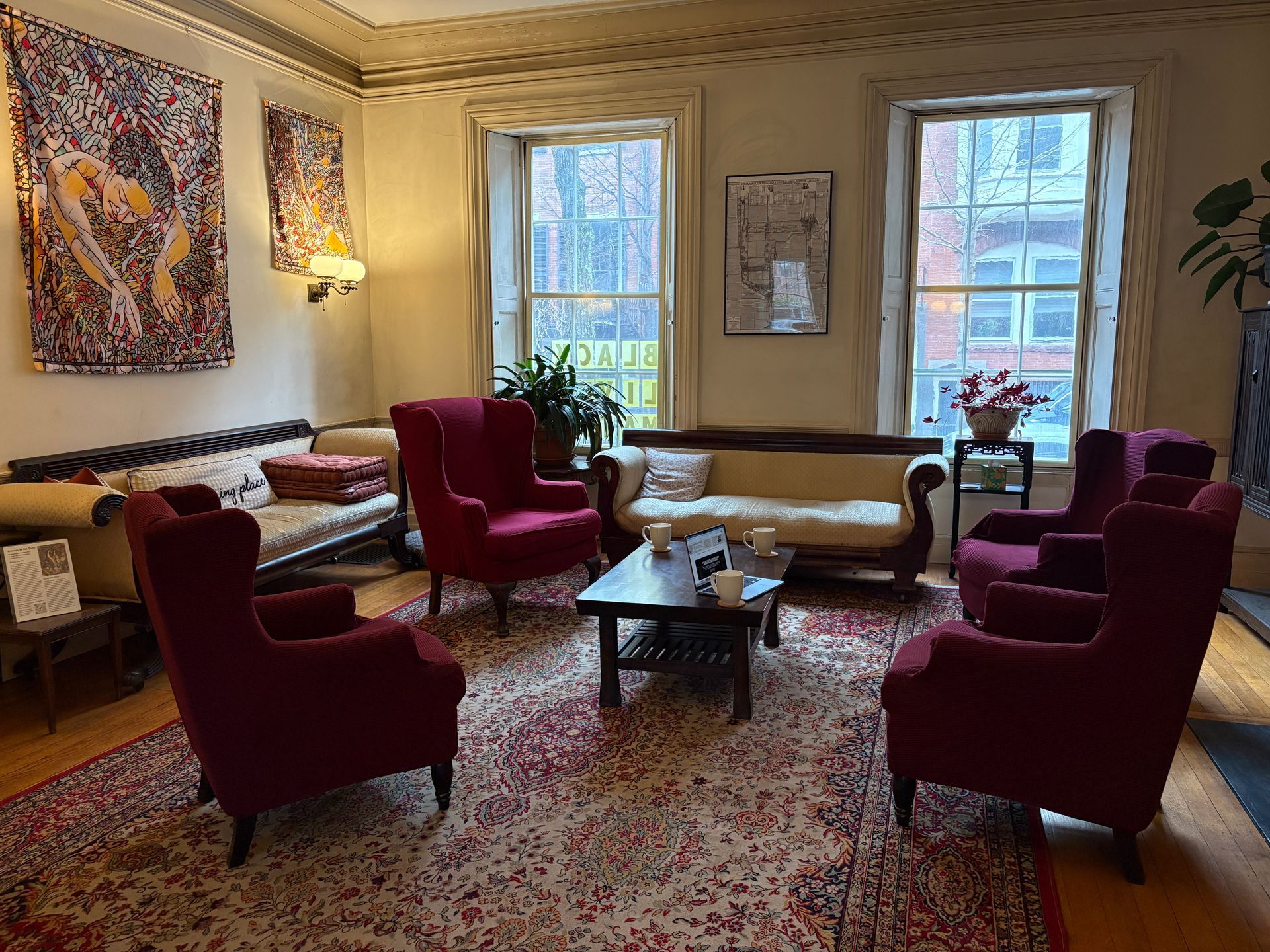 A living room featuring several dark red wingback chairs, a neutral couch, and a patterned rug on a wood floor.
