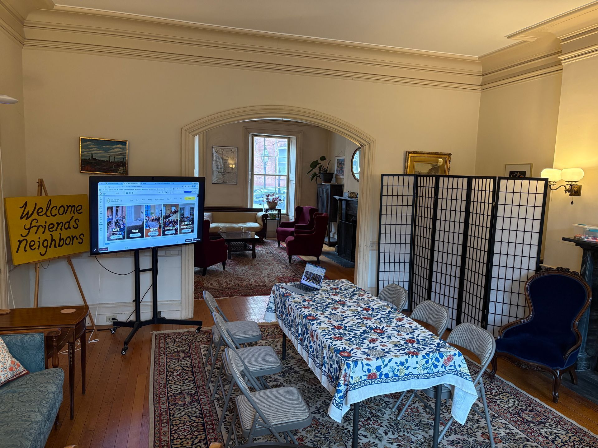A room set up for a presentation with a television on a stand, a table with chairs, and a folding screen.
