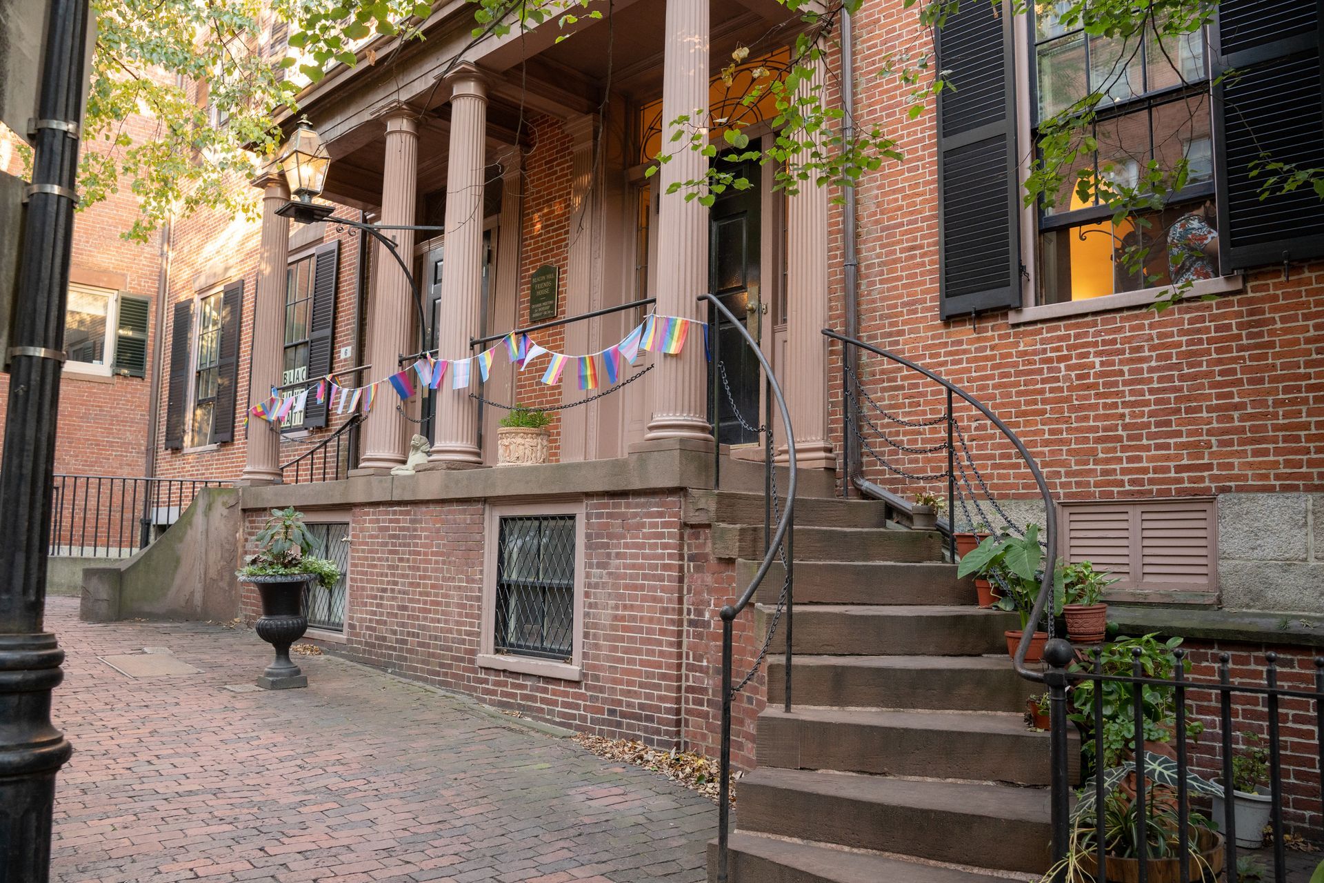 Brick building with a columned porch, curved stone staircase, black shutters, and decorative pennant flags strung across.
