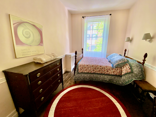 A bright bedroom with a dark wood dresser, a bed with a floral quilt, and a red circular rug on the wooden floor.