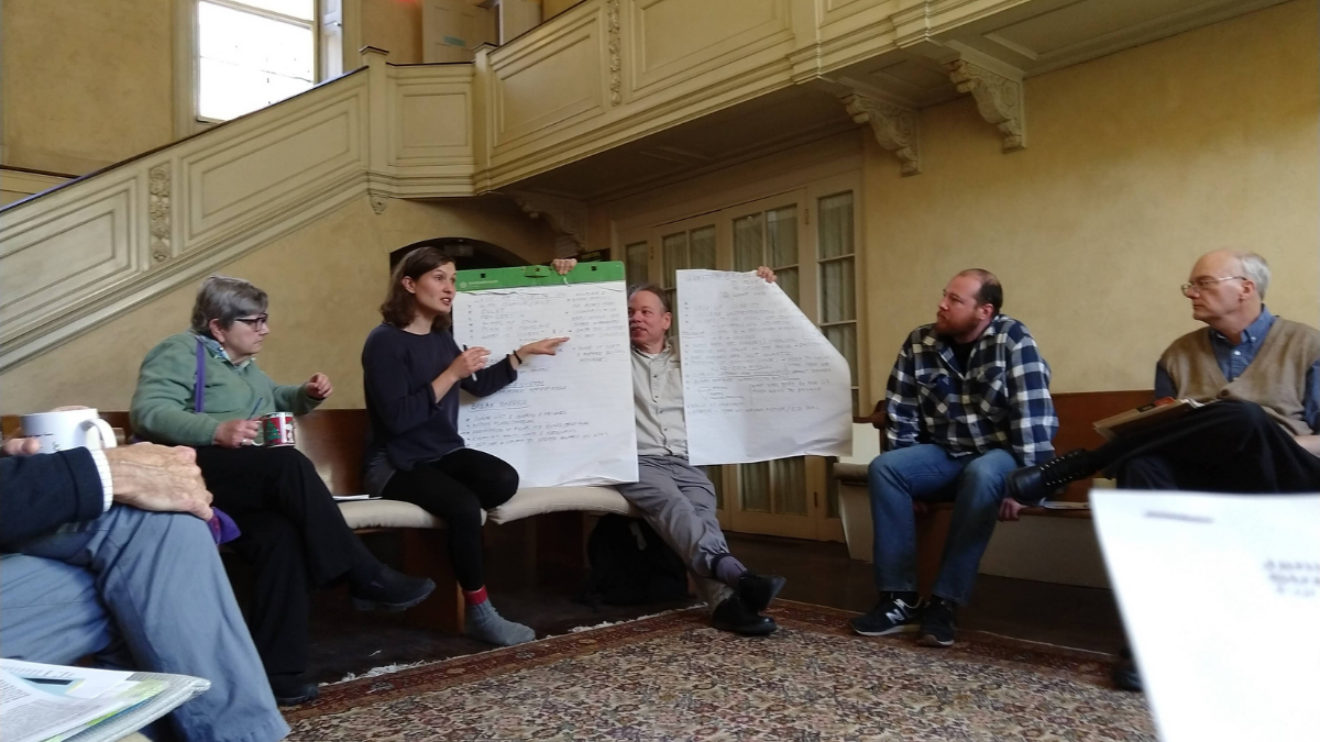 People sitting in a circle in a large room, two holding up charts while discussing them.