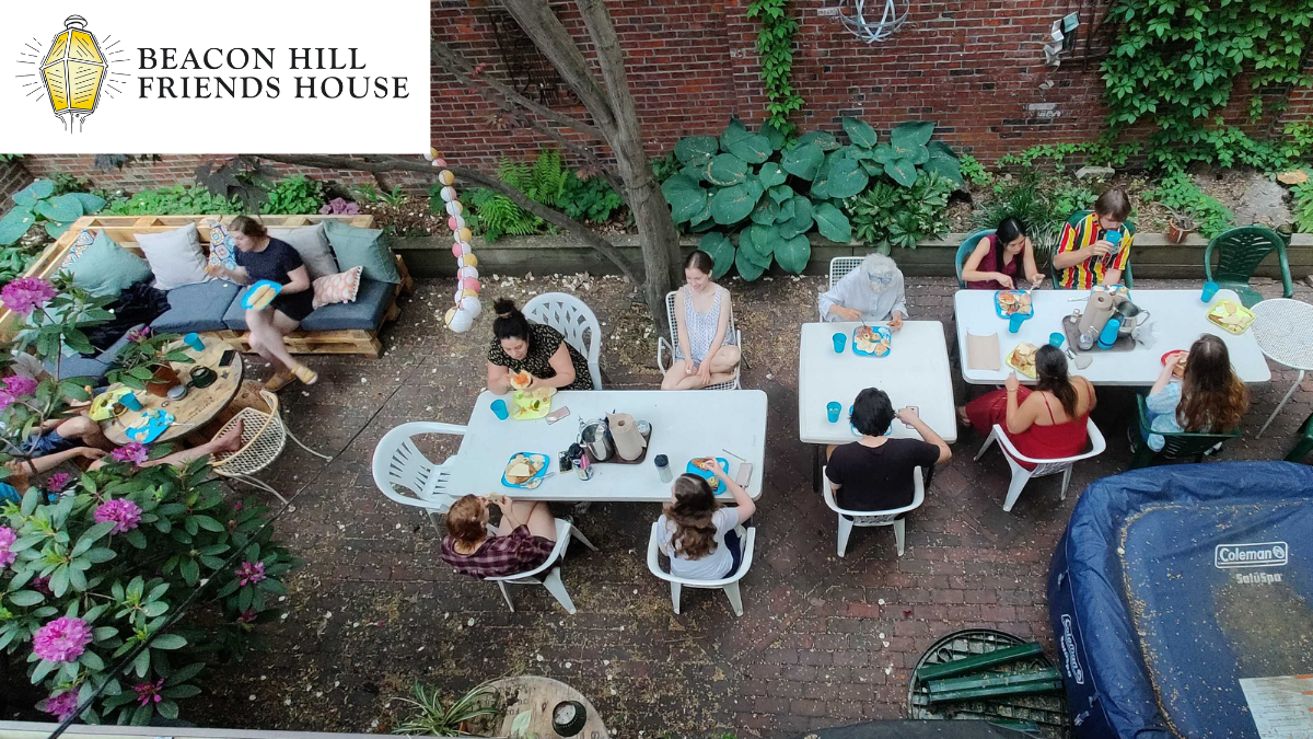 A high-angle view of a garden gathering with people seated at tables, a patio lounge, and a blue pool on a brick patio.