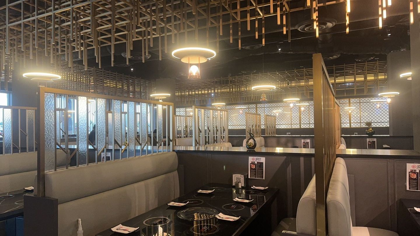 JPOT Japanese hot pot & BBQ restaurant interior with gray and black booths, tables and gold lighting and ceiling structures