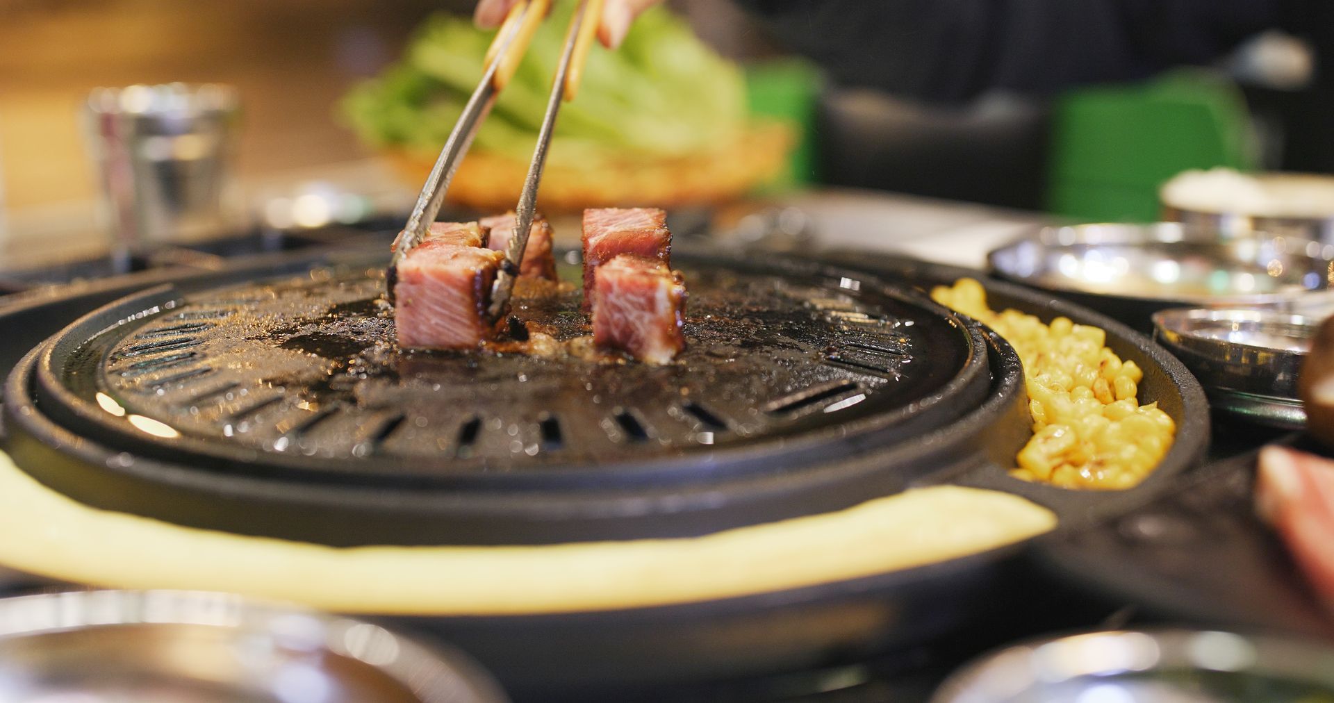 JPOT Japanese BBQ hand using tongs to grill cubed meat on a BBQ grill on table