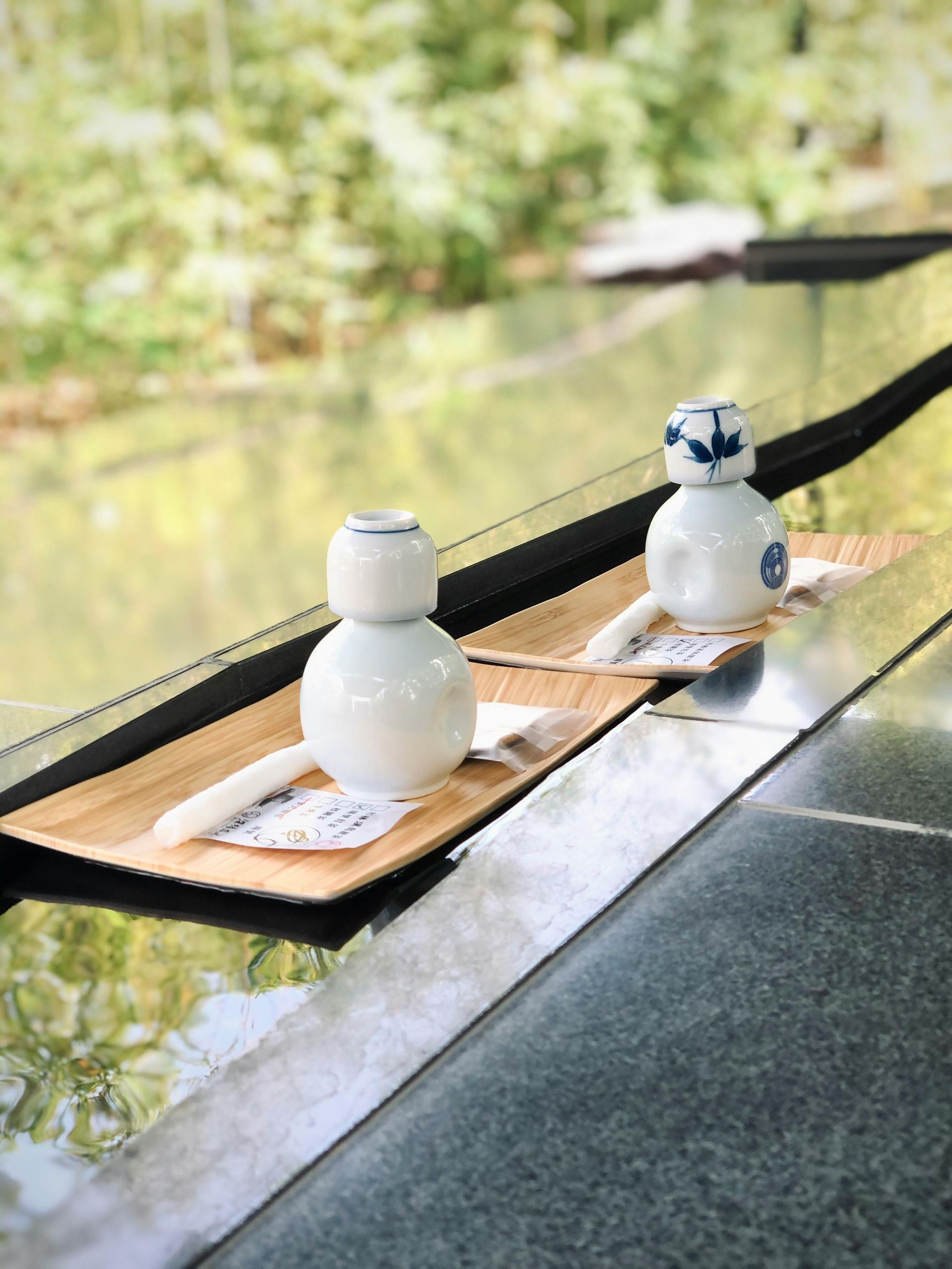 JPOT Japanese sake in two white flasks on wooden trays on a granite bar