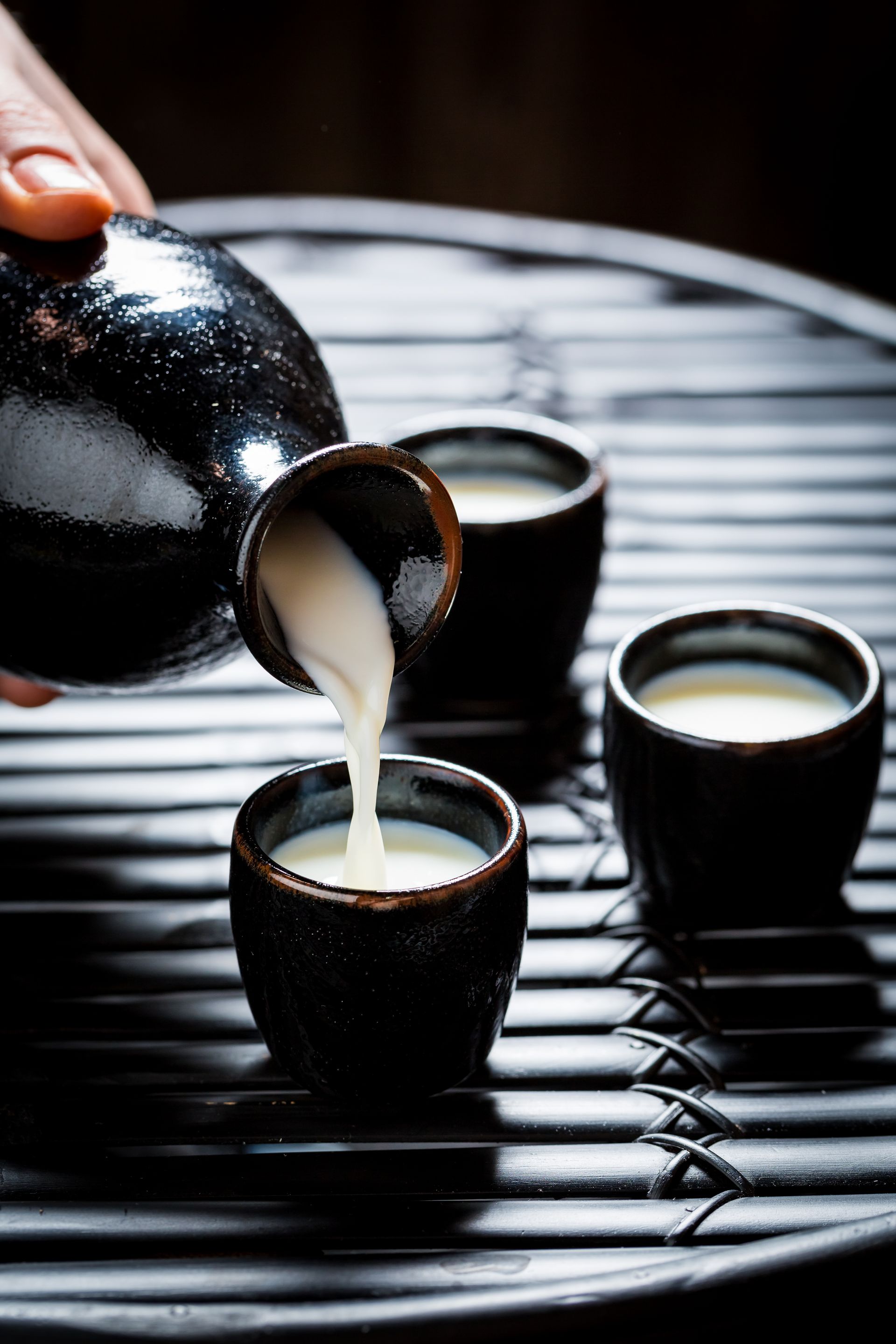 JPOT Sake being poured from a black sake flask into 3 matching black ceramic cups