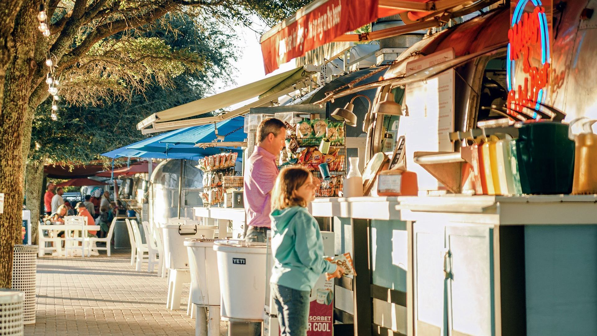 A man and a girl are standing in front of a food truck.
