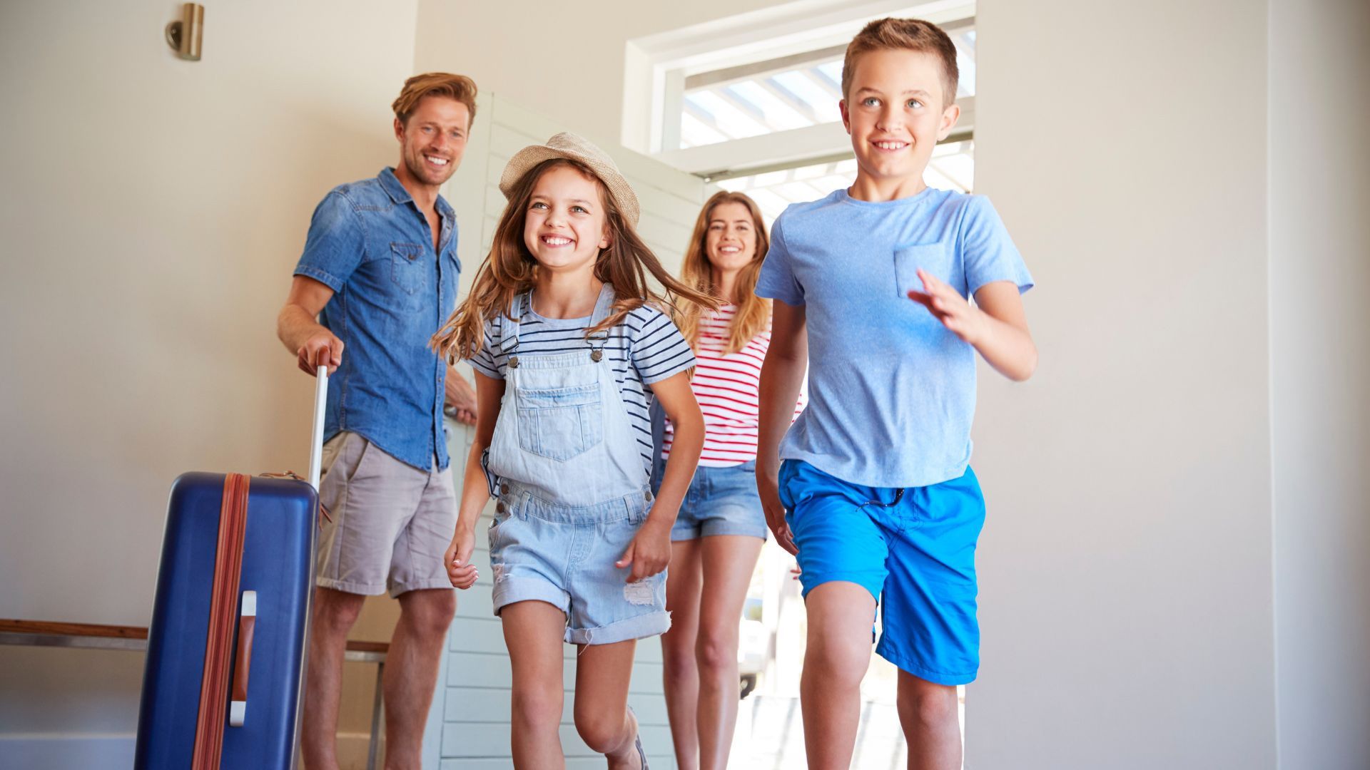 A family is walking into a house with luggage.