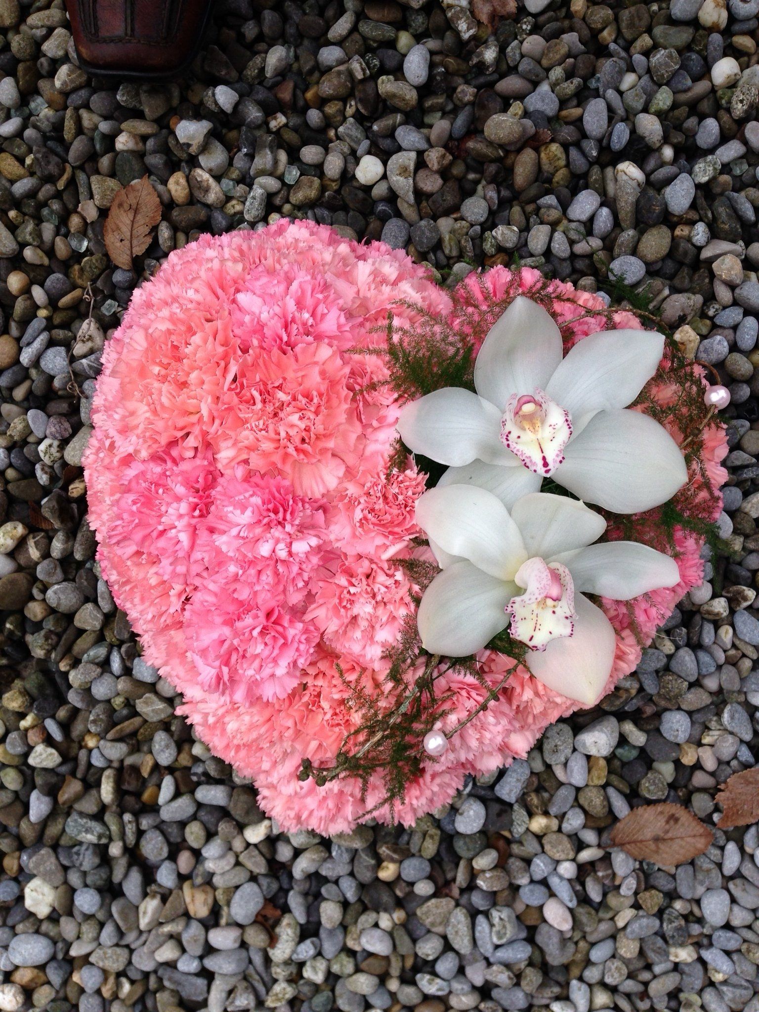 Auf einem Steinhaufen liegt ein Herz aus rosa und weißen Blumen.