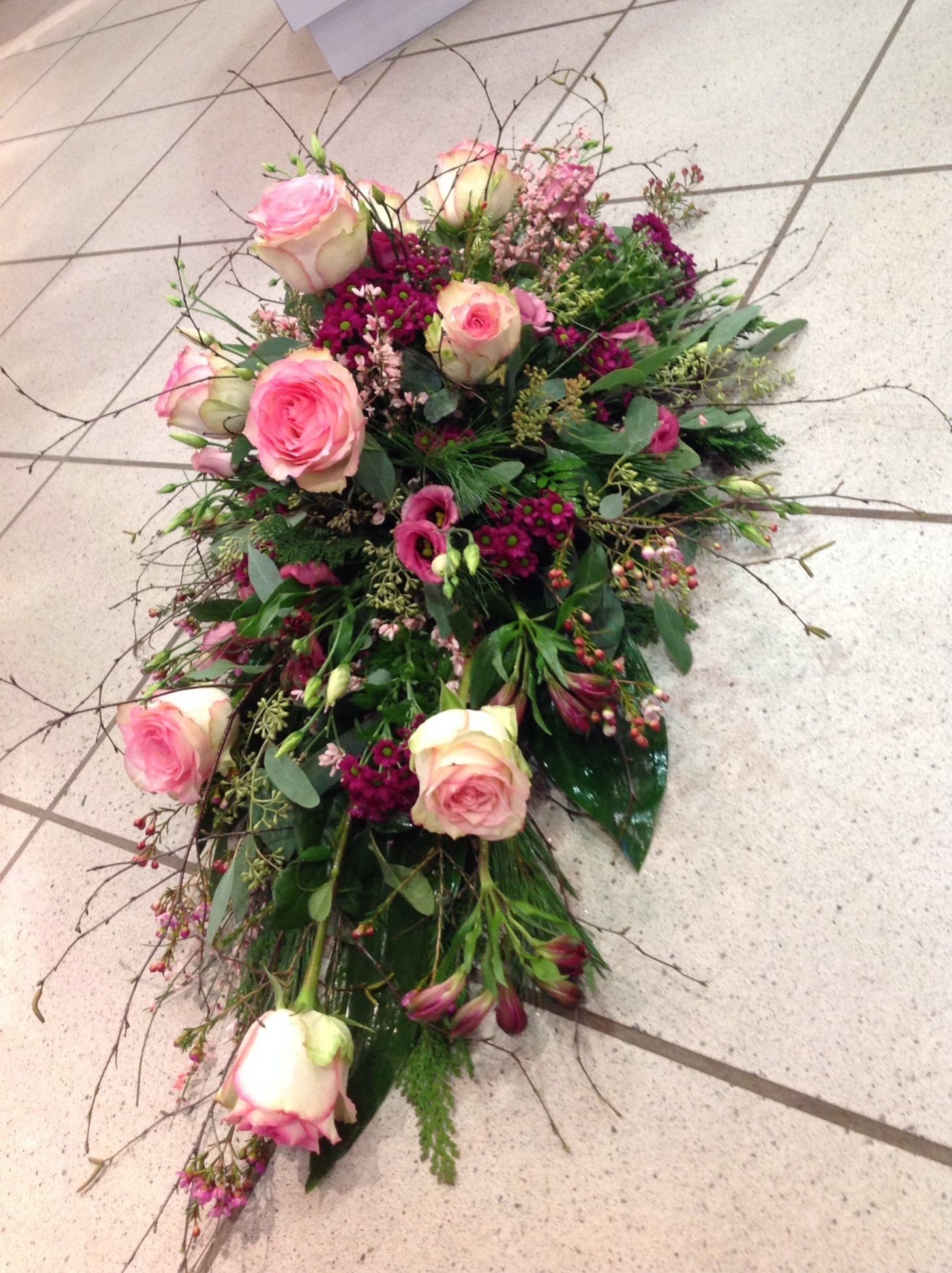 Auf einem gefliesten Boden liegt ein Strauß rosa und violetter Blumen.