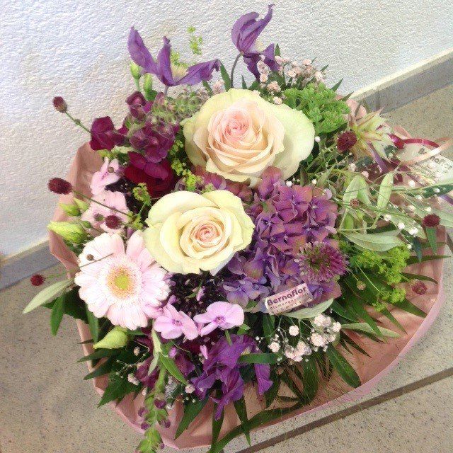 Ein Strauß rosa und lila Blumen ist in rosa Papier eingewickelt