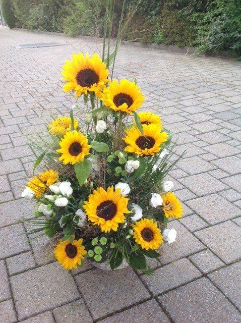Ein Korb mit Sonnenblumen und weißen Blumen auf einem gemauerten Gehweg