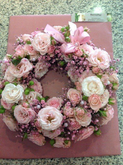 Auf einem Tisch steht ein Kranz aus rosa und weißen Blumen.