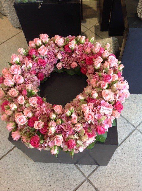 Ein Kranz aus rosa Blumen sitzt auf einer schwarzen Kiste
