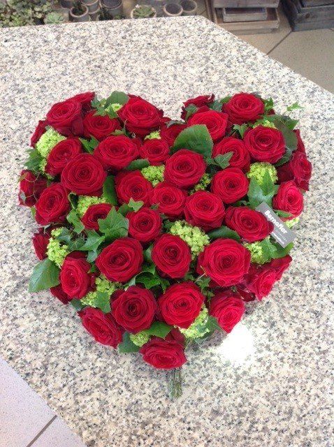 Ein herzförmiges Arrangement aus roten Rosen und Grünpflanzen