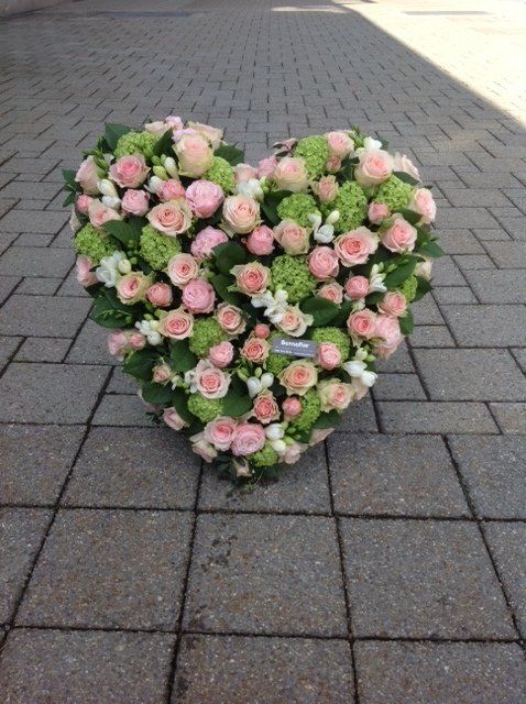 Ein herzförmiges Arrangement aus rosa und grünen Blumen auf einem gemauerten Gehweg