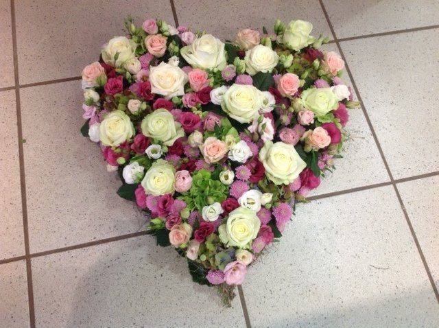 Auf einem gefliesten Boden steht ein herzförmiges Blumenarrangement.