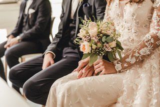 Bei einer Hochzeitszeremonie sitzen Braut und Bräutigam nebeneinander und halten Händchen.
